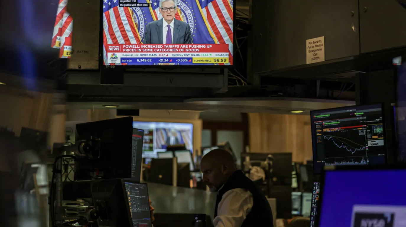 Một nhà giao dịch trên sàn NYSE đang làm việc dưới một màn hình phát sóng bản tin về cuộc họp báo của Chủ tịch Fed Jerome Powell ngày 30/7/2025 - Ảnh: Reuters.