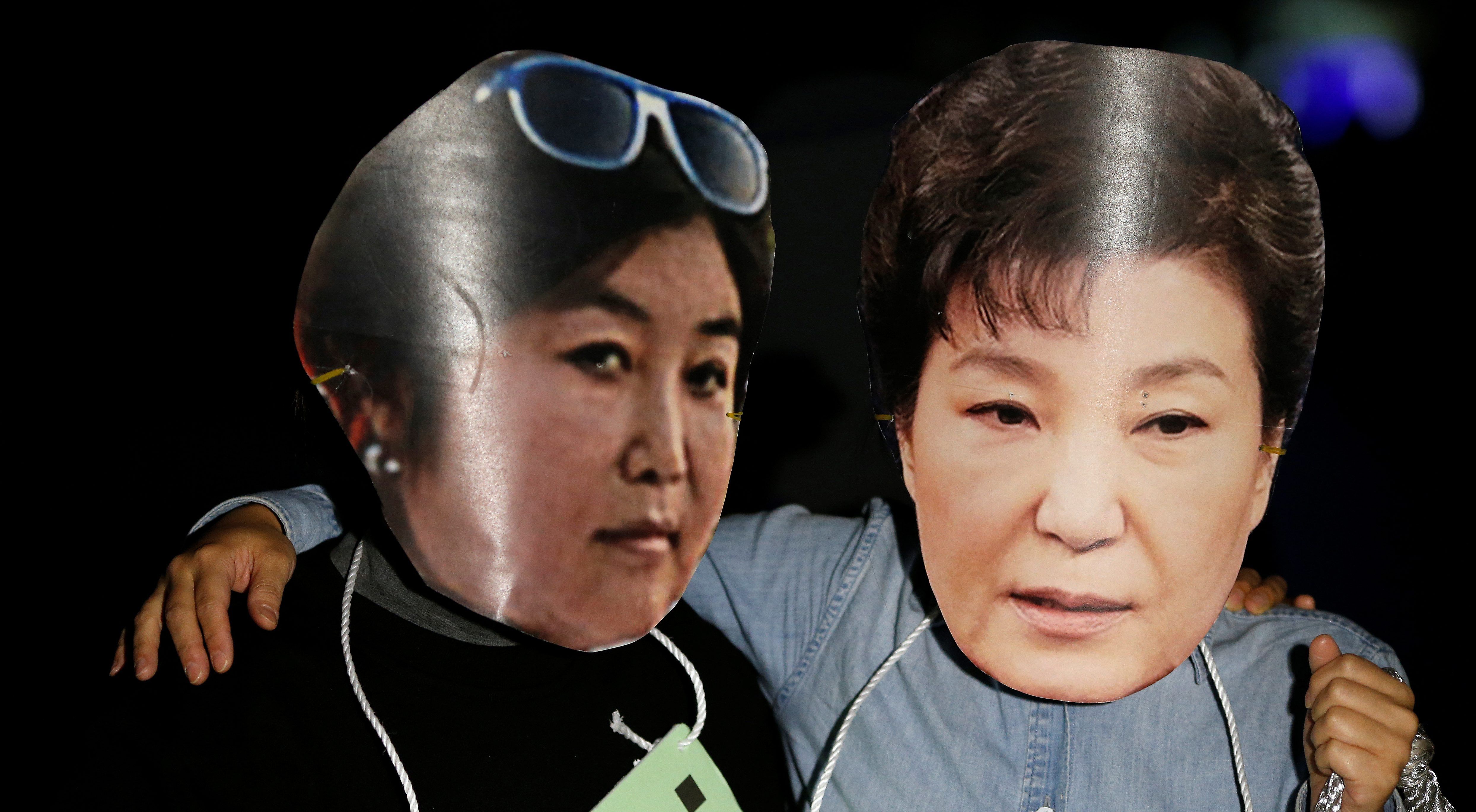 Người biểu tình ở Seoul, Hàn Quốc đeo mặt nạ cắt từ ảnh của bà Choi Soon-sil (trái) và ảnh cuẩ Tổng thống Park Geun-hye - Ảnh: Reuters.<br>