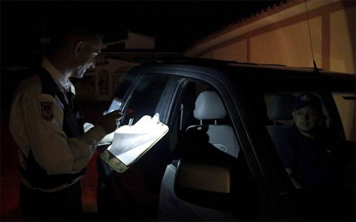 Một nhân viên an ninh Venezuela dùng điện thoại để làm đèn chiếu sáng khi làm việc tại một chốt kiểm soát trong lúc đang mất điện - Ảnh: Reuters.<br>