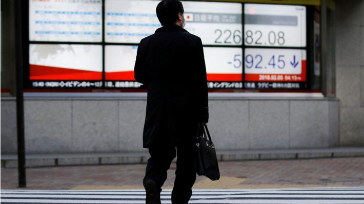 Một người đàn ông đi qua một bảng giá chứng khoán trên đường phố ở Tokyo, Nhật Bản sáng 5/2 - Ảnh: Reuters.