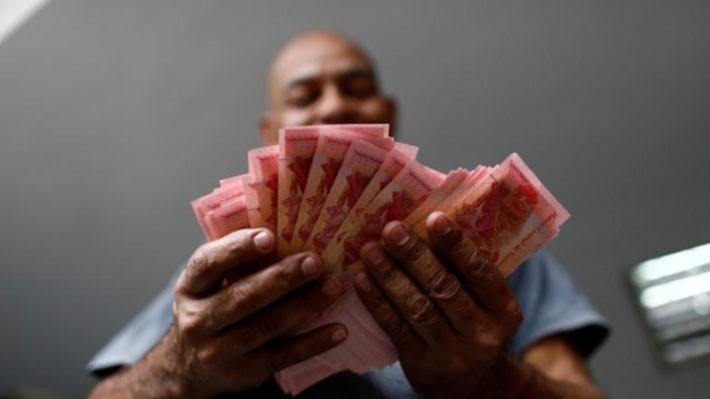 Nhân viên một bãi đỗ xe ở thủ đô Caracas của Venezuela đang đềm tiền là đồng nội tệ Bolivar - Ảnh: Reuters.