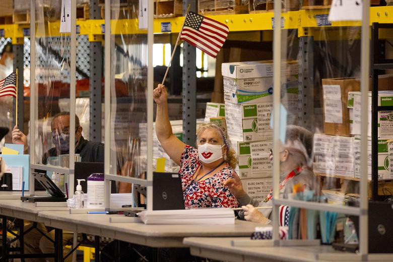 Nhân viên bầu cử vẫy cờ mời cử tri tại một điểm bỏ phiếu ở San Diego, California - Ảnh: Reuters.