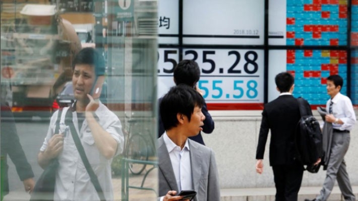 Những người bộ hành đi qua một bảng điện tử trên đường phố Tokyo hiển thị diễn biến chỉ số Nikkei của chứng khoán Nhật Bản phiên ngày 12/10 - Ảnh: Reuters.