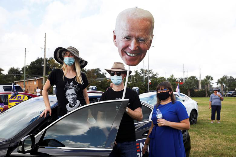Những người ủng hộ ông Biden cầm biển với khuôn mặt của ứng viên đảng Dân chủ tại khu vực đỗ xe của sự kiện vận động tranh cử do cựu Tổng thống Barack Obama chủ trì thay mặt ông Biden ở Orlando, Florida, ngày 27/10.