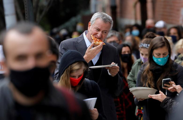 Thị trưởng thành phố New York Bill de Blasio tranh thủ ăn pizza khi đứng xếp hàng cùng hàng trăm cử tri khác để bỏ phiếu sớm ở quận Brooklyn, New York ngày 27/10.