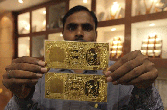 Nhân viên tại một tiệm vàng ở thành phố Lucknow, Ấn Độ, trưng hai miếng vàng phỏng theo hình ảnh đồng Rupee của nước này - Ảnh: Reuters/Daylife.