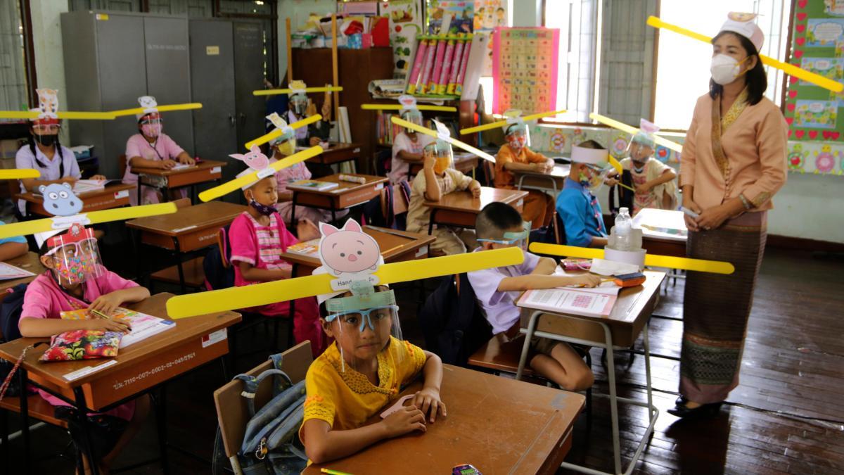 Giáo viên và học sinh tại một trường học ở Chiang Mai, Thái Lan đội mũ có tấm kính chắn giọt bắn và thước kẻ dài để duy trì giãn cách - Ảnh: AP