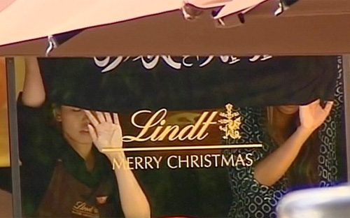 Những kẻ bắt cóc ép các con tin nữ đứng gần cửa sổ và cầm cờ Hồi giáo màu đen - Ảnh: Seven News.<br>