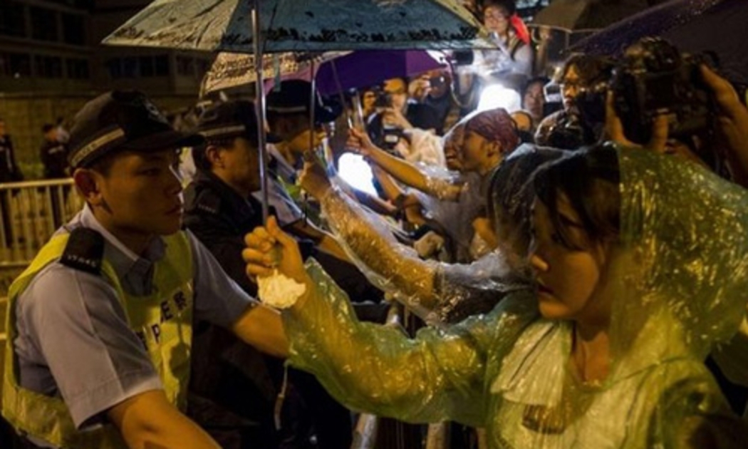 Người biểu tình Hồng Kông cầm ô che mưa cho cảnh sát - Ảnh: AFP.