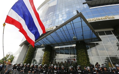 Một người biểu tình Thái Lan vẫy cờ trước hàng rào cảnh sát đứng bảo vệ một cơ sở truyền thông ở Bangkok ngày 9/5 - Ảnh: EPA.<br>