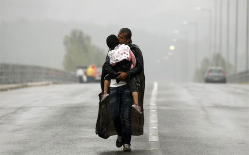 Một người di cư Syria bế đứa con nhỏ trên tay chuẩn bị vượt qua biên giới Hy Lạp-Macedonia từ một ngôi làng gần biên giới của Hy Lạp ngày 10/9 - Ảnh: Reuters.<br>
