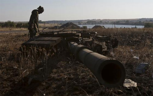 Một tay súng phe ly khai Ukraine đứng cạnh chiếc xe tăng đã bị phá nát - Ảnh: Reuters.<br>