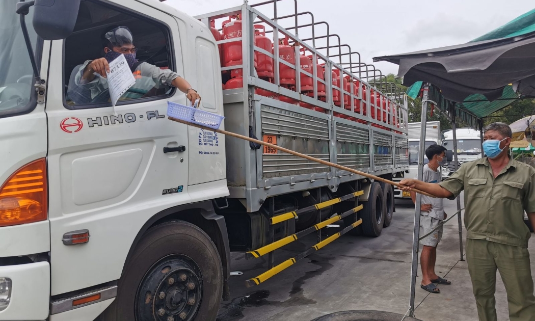 Các phương tiện vận chuyển hàng thiết yếu trình giấy tờ để kiểm soát  tại bãi tập kết hàng hóa, trạm thu phí T2, quận Cái Răng. Ảnh: Báo Cần Thơ