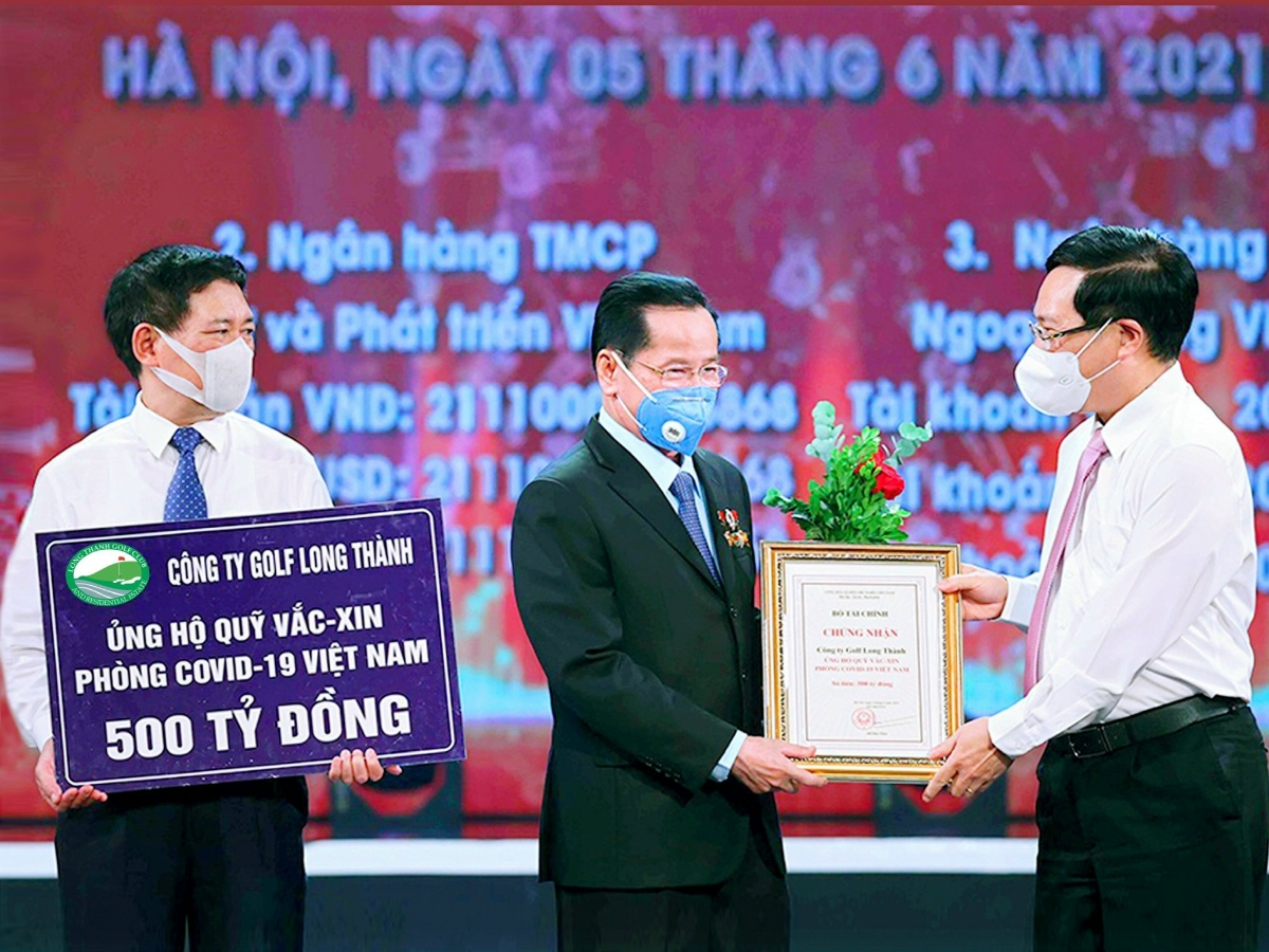 Doanh nh&acirc;n cựu chiến binh AHLĐ L&ecirc; Văn kiểm Chủ tịch HĐQT c&ocirc;ng ty Golf Long Th&agrave;nh đ&atilde; trao tặng quỹ vắc xin ph&ograve;ng, chống Covid-19 số tiền 500 tỉ đồng. Ủy vi&ecirc;n Bộ Ch&iacute;nh Trị, Ph&oacute; Thủ tướng Phạm B&igrave;nh Minh trao giấy chứng nhận v&agrave; hoa, Bộ trưởng Bộ T&agrave;i Ch&iacute;nh Hồ Đức Phớc nhận bảng ủng hộ 500 tỉ đồng.