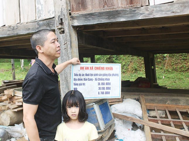 Anh Trung nhặt tấm biển của Tiểu dự &aacute;n nu&ocirc;i lợn nằm lăn l&oacute;c dưới nền đất.