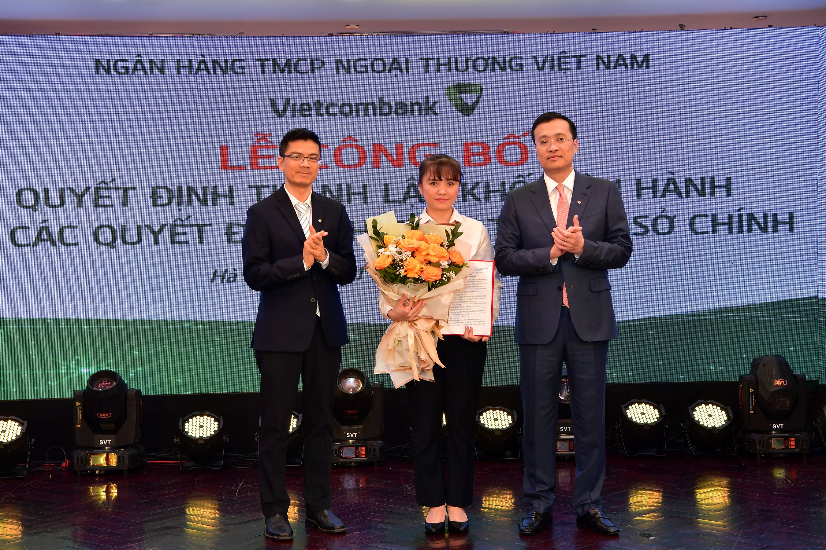 Ông Phạm Quang Dũng - Chủ tịch HĐQT (bên phải) trao quyết định và ông Trần Thanh Nam - Giám đốc Khối Vận hành (bên trái) tặng hoa chúc mừng bà Thái Thị Thu Hằng - tân Phó trưởng phòng phụ trách Phòng Quản lý chất lượng - Trụ sở chính Vietcombank.
