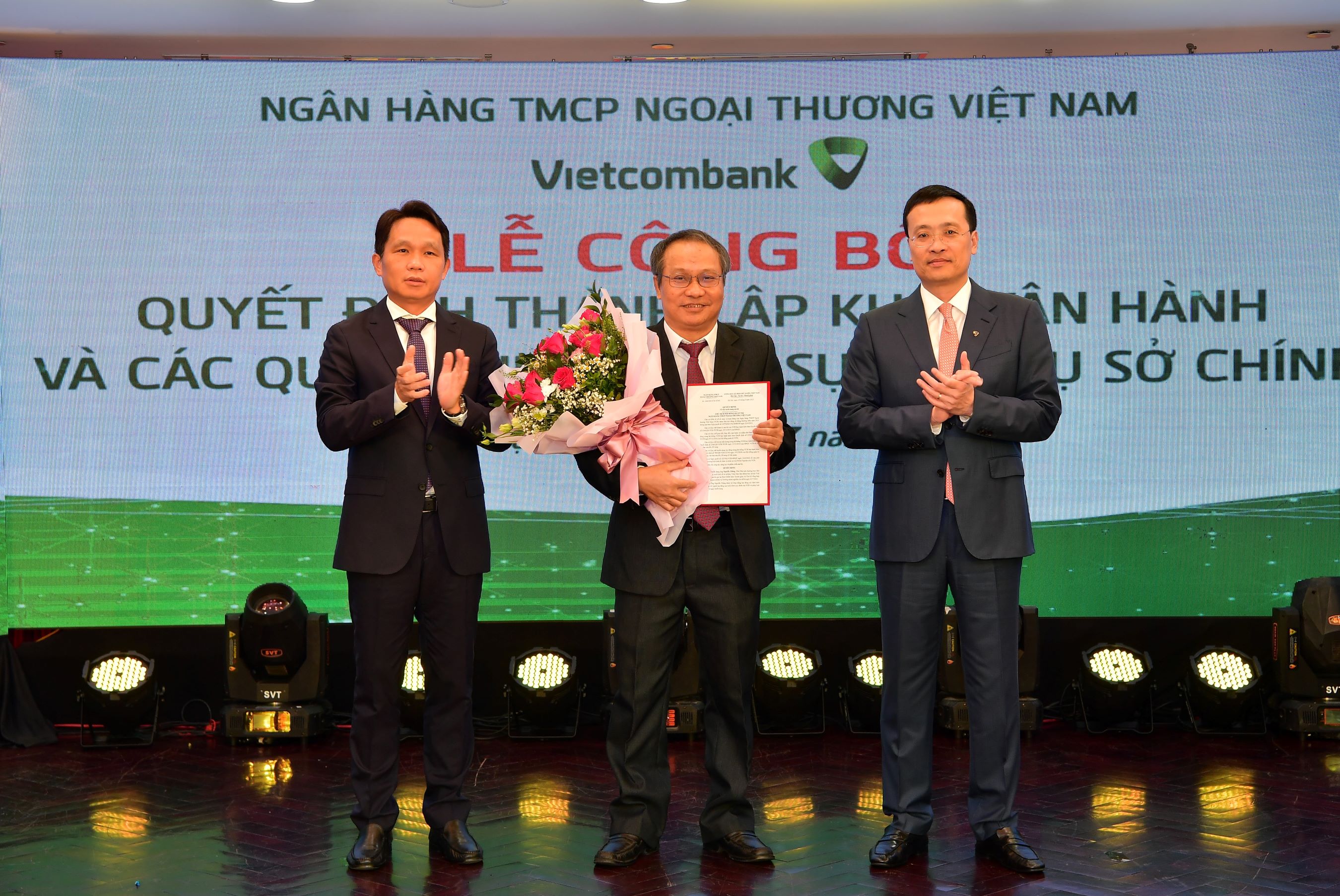 Ông Phạm Quang Dũng - Chủ tịch HĐQT (bên phải) trao quyết định và ông Nguyễn Mạnh Hùng - Thành viên HĐQT tặng hoa chúc mừng tân Trưởng nhóm Nghiên cứu Vietcombank - Tiến sỹ Nguyễn Thắng.