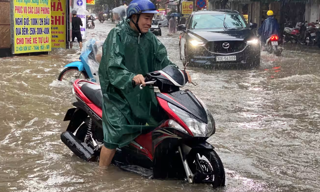 Một người đàn ông lái xe máy trên đường phố bị ngập ở Hà Nội sau trận mưa lớn vào tháng 9/2023 - Ảnh: Reuters