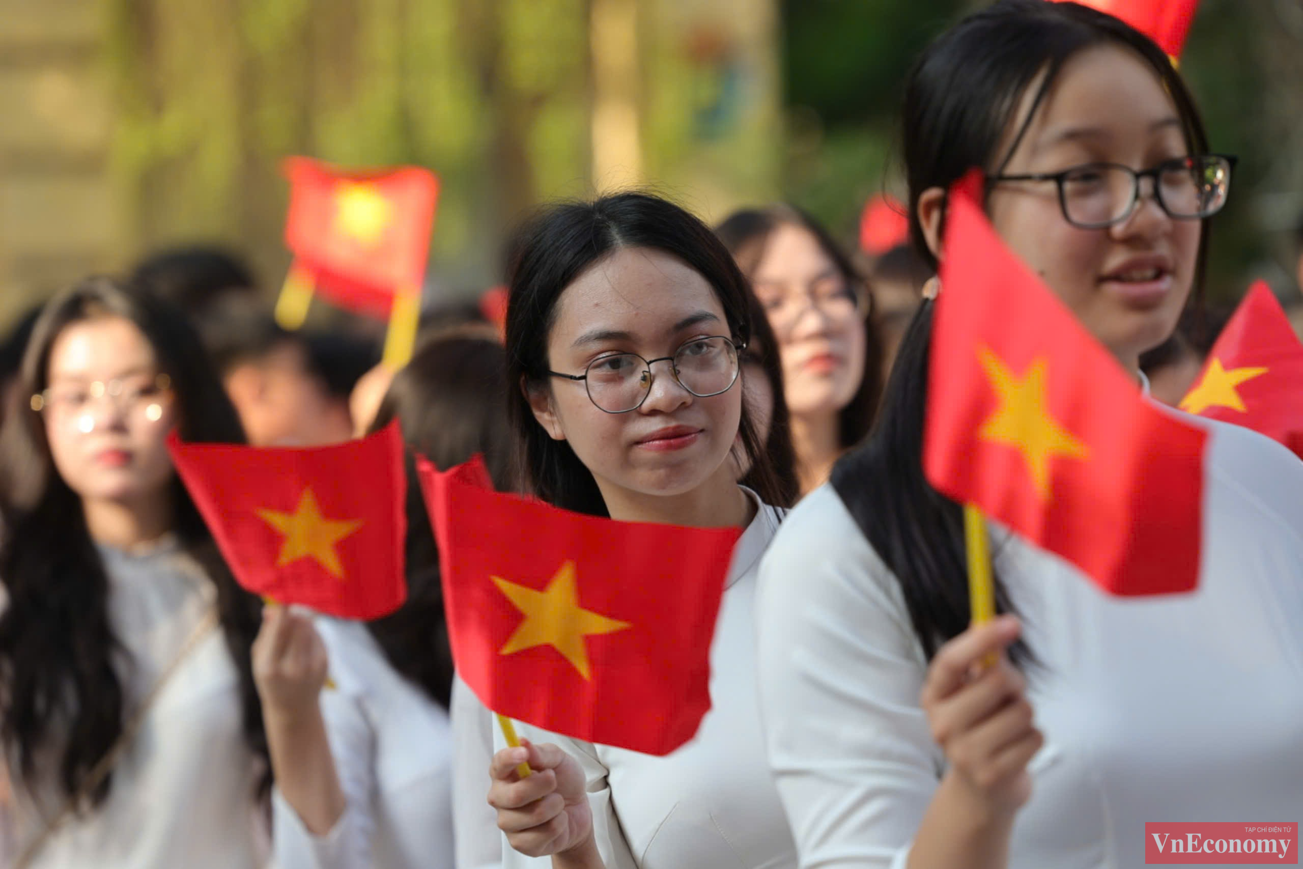 Tại trường PTTH Việt Đức, c&aacute;c nh&oacute;m nữ sinh mặc &aacute;o d&agrave;i trắng tay cầm cờ đỏ tiến v&agrave;o trường đ&atilde; thu h&uacute;t &aacute;nh nh&igrave;n của người đi đường.