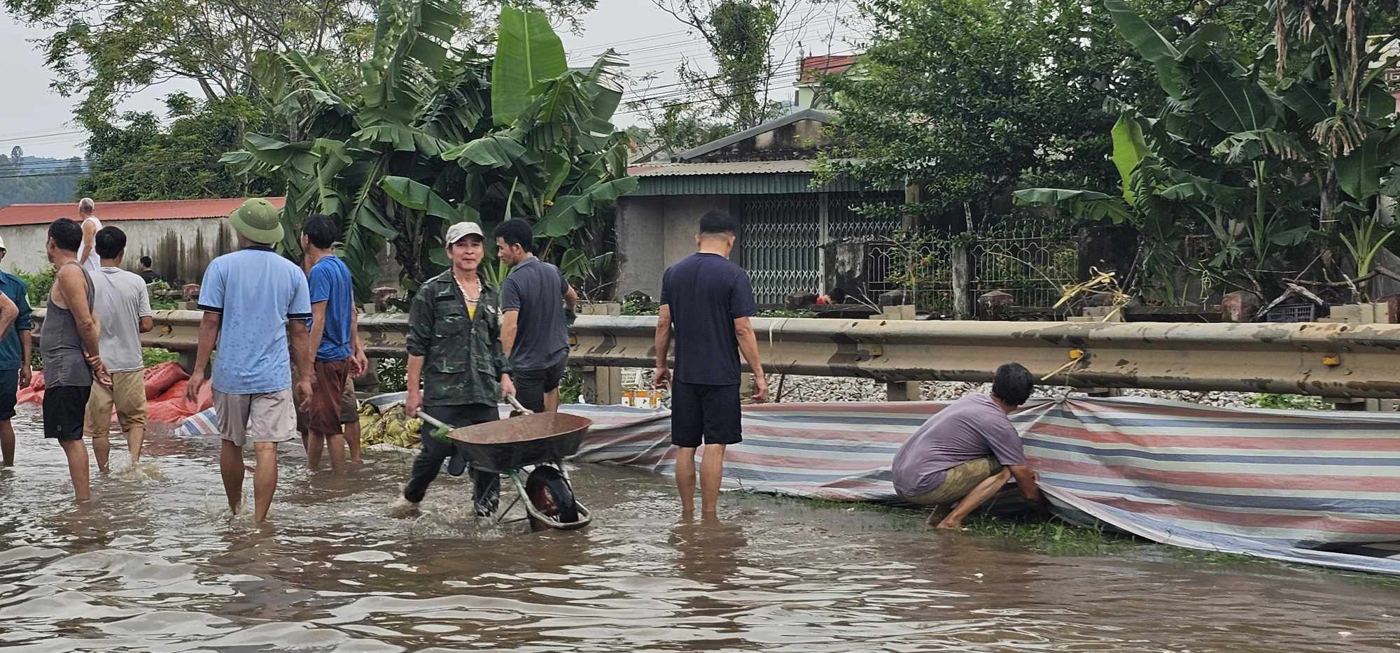 Người d&acirc;n d&ugrave;ng bao tải v&agrave; bạt để ngăn nước từ quốc lộ chảy v&agrave;o khu d&acirc;n cư
