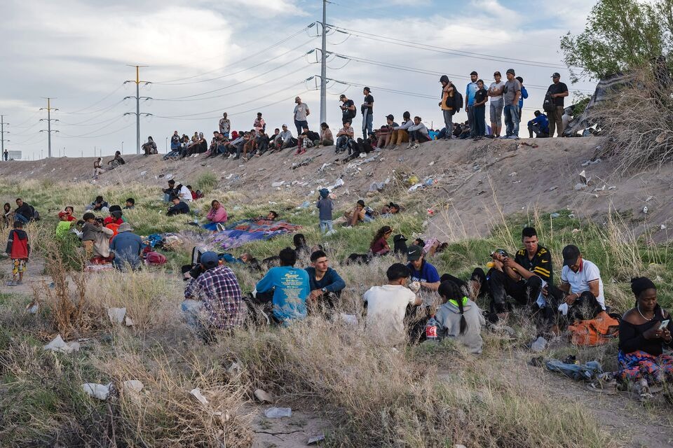 Người di cư ngồi bên bờ sông Rio Grande tại biên giới Mỹ-Mexico ở Ciudad Juarez, Mexico vào tháng 4 - Ảnh:Bloomberg