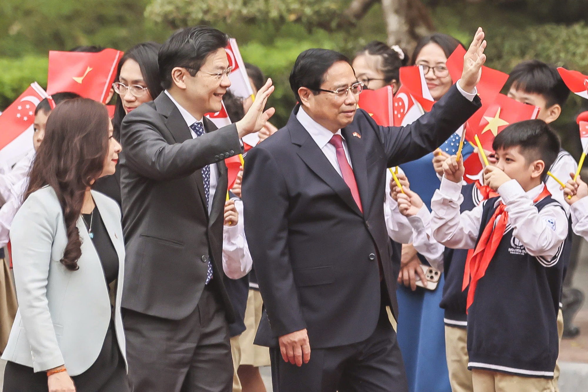 Hai Thủ tướng bước tr&ecirc;n thảm đỏ trong tiếng vẫy ch&agrave;o của c&aacute;c em học sinh với quốc kỳ Việt Nam v&agrave; Singapore tr&ecirc;n tay - Ảnh: VGP