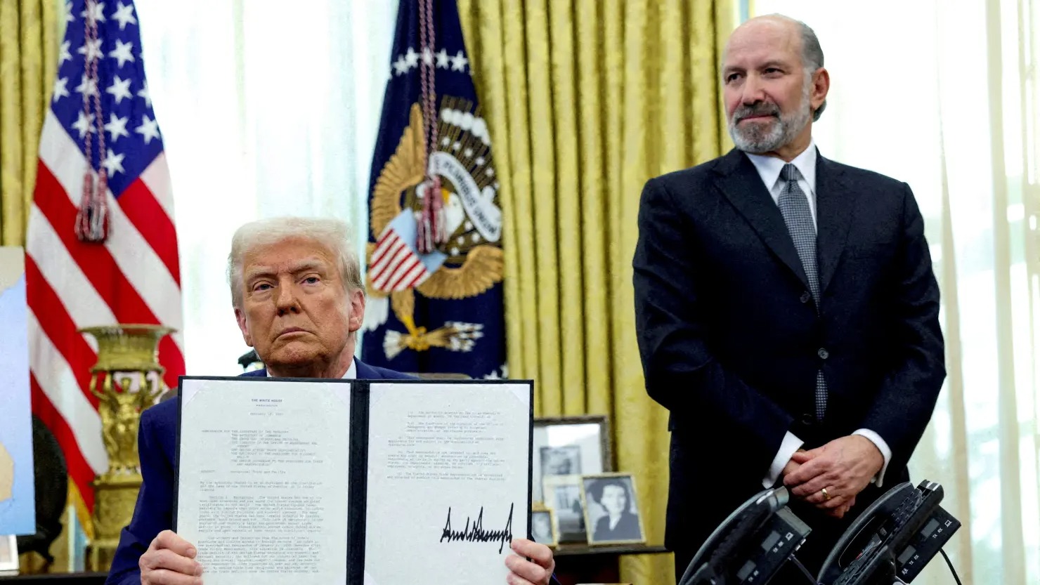 Tổng thống Donald Trump cầm một sắc lệnh hành pháp về việc tăng thuế quan, bên cạnh là Bộ trưởng Thương mại Hoa Kỳ Howard Lutnick, tại Phòng Bầu dục của Nhà Trắng ở Washington, D.C., hồi tháng 2. Ảnh: Reuters