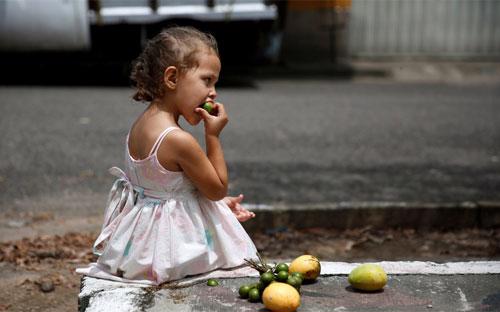 Một bé gái ăn hoa quả trên đường phố ở La Fria, Venezuela hôm 2/6/2016 - Ảnh: Reuters.<br>