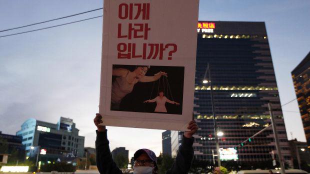 Người biểu tình ở Seoul, Hàn Quốc giơ bức tranh mô phỏng Tổng thống Park Geun-hye đang bị Choi Soon-sil điều khiển như một con rối - Ảnh: Getty.<br>