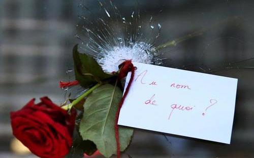 Bông hồng đính kèm một tờ giấy nhỏ đặt xuyên qua vết đạn mà vụ khủng bố đêm 13/11 để lại trên cửa sổ một nhà hàng ở Paris, Pháp. Trên tờ giấy viết: "Nhân danh điều gì?" - Ảnh: Reuters.<br>