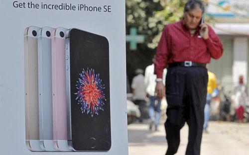 Một người đàn ông bước đi gần một biển quảng cáo iPhone SE ở New Delhi, Ấn Độ - Ảnh: Reuters.<br>