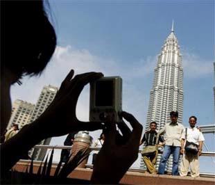 Một người lao động nhập cư chụp ảnh lưu niệm cho bạn, phía trước tòa tháp đôi Petronas tại Kuala Lumpur (Malaysia) - Ảnh: AP.