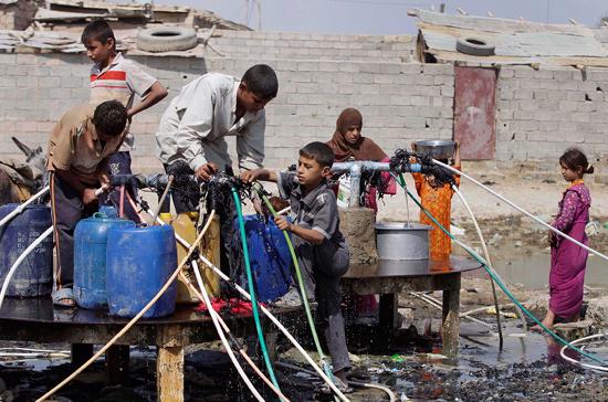 Những cậu bé Iraq ở ngoại ô thủ đô Baghdad đang cố gắng đổ đầy nước vào thùng - Ảnh: AP. 