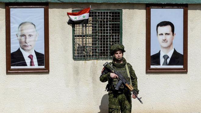 Ảnh Tổng thống Nga Vladimir Putin (trái) và ảnh Tổng thống Syria Bashar al-Assad trước một tòa nhà ở Syria - Ảnh: Getty/BBC.