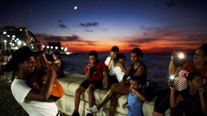 Một người phụ nữ và một bé gái dùng điện thoại di động quay video màn biểu diễn của một nghệ sỹ đường phố bên bờ biển ở Havana, Cuba - Ảnh: Reuters.