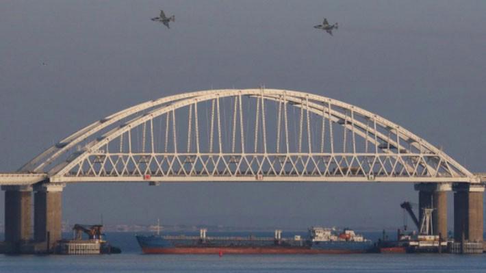 Chiến đấu cơ của Nga bay phía trên cây cầu nối giữa đại lục Nga với Crimea ngày 25/11. Bên dưới cầu là một con tàu chở hàng đứng chắn, sau khi lực lượng của Nga bắt giữ ba chiến hạm Ukraine - Ảnh: Reuters.