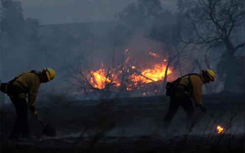 Lính cứu hỏa đang cố gắng dập một đám cháy rừng ở Quận Cam, California, ngày 9/10 - Ảnh: Reuters.<br>