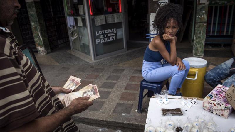 Một người đàn ông đếm tiền trước khi mua đường và cà phê đóng gói nhỏ tại một khu phố của Caracas, Venezuela vào tháng 4/2018 - Ảnh: Bloomberg.