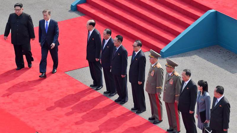 Nhà lãnh đạo Triều Tiên Kim Jong Un và Tổng thống Hàn Quốc Moon Jae-in bước đi trên thảm đỏ, bên cạnh là các quan chức Triều Tiên tháp tùng ông Kim Jong Un tới Hàn Quốc - Ảnh: Bloomberg.