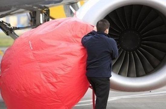 Một nhân viên hàng không đang tìm cách che bụi lọt vào động cơ máy bay - Ảnh: AFP.