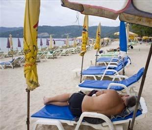 Một du khách phương Tây nằm tắm nắng trên bãi biển Patong, đảo Phuket (Thái Lan). Dự kiến, số du khách nước ngoài tới Thái Lan trong tháng 12 này sẽ là 500.000 người, chỉ bằng 1/3 so với dự báo ban đầu - Ảnh: AP.