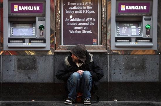 Một người đàn ông ngồi co ro giữa hai chiếc máy ATM tại Dublin, thủ đô Ireland. Lợi suất trái phiếu Chính phủ Ireland đã tăng vọt, đe dọa khả năng tiếp tục huy động tài chính của Dublin, đẩy quốc gia đang bị đè nặng bởi nợ công và thâm hụt ngân sách này tới bờ vực vỡ nợ - Ảnh: Reuters. 