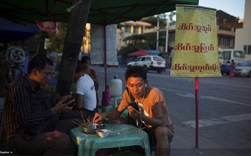 Sóng Viettel sắp chính thức phủ lên đất Myanmar. Trong ảnh là một người đàn ông Myanmar sử dụng điện thoại di động khi đang ngồi quán vỉa hè ở Yangon -&nbsp;Ảnh: Bloomberg.