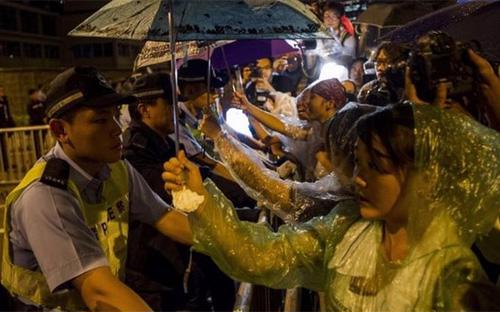 Người biểu tình Hồng Kông cầm ô che mưa cho cảnh sát - Ảnh: AFP.<br>