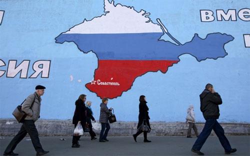 Khách bộ hành ở Moscow đi qua một bức tường có vẽ bản đồ Crimea - Ảnh: Bloomberg.<br>