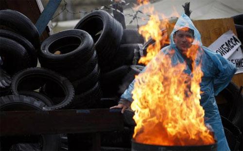 Một người biểu tình thân Nga sưởi ấm bên đống lửa đốt gần một barrier bên ngoài một tòa nhà công quyền ở thành phố Donetsk thuộc miền Đông Ukraine hôm 20/4 - Ảnh: Reuters.