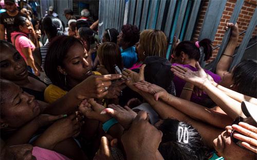 Người Venezulea chìa tay để được đánh số thứ tự vào mua hàng tại một cửa hàng thực phẩm ở Caracas hồi tháng 2 - Ảnh: Bloomberg.<br>