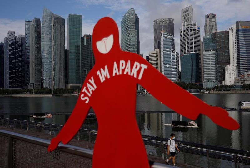 Một người đàn ông đeo khẩu trang đi qua một tấm biển được dựng lên để khuyến khích giãn cách xã hội trong đợt bùng phát dịch tại Vịnh Marina ở Singapore - Ảnh: Reuters