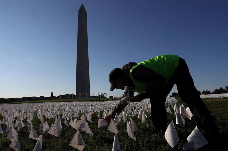 Một tình nguyên viên cắm cờ trắng tại đài tưởng niệm những người đã tử vong vì Covid-19, nằm bên cạnh Đài tưởng niệm Washington ở Washington, Mỹ ngày 1/10 - Ảnh: Reuters
