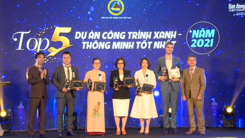 A representative from the Phuc Khang Corporation (dressed in an ao dai) receives the trophy and certificate for Top 5 best smart green building project in 2021.